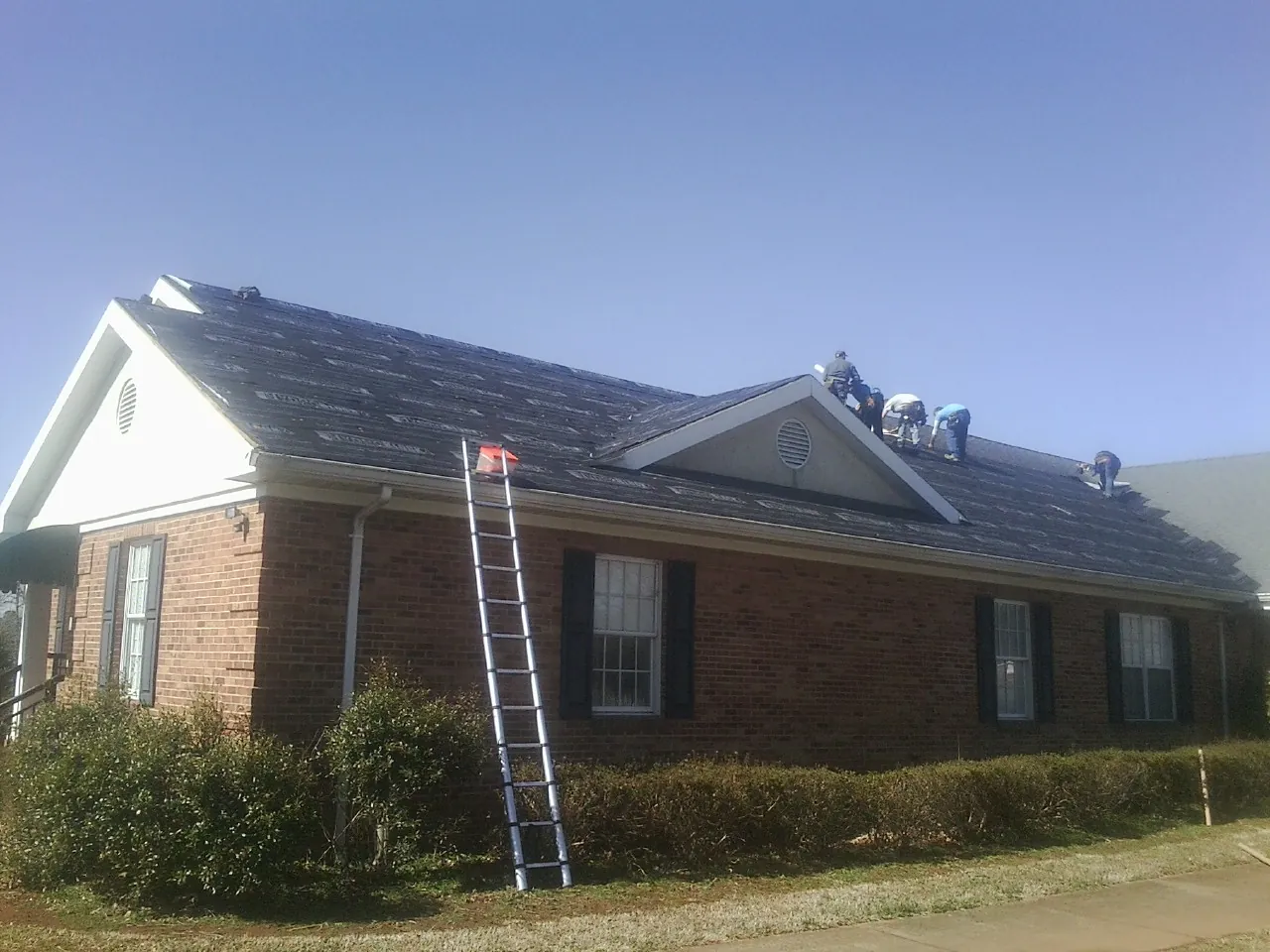 Crew tearing shingles off a brick ranch roof with a ladder set — Emergency Roof Repair work by our crew in Allison