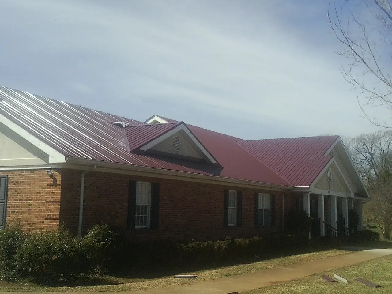 Red metal roof with gabled entries on a long brick building, from a Hail Damage Roof Repair job in Allison