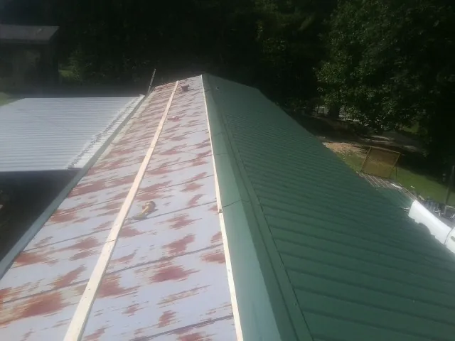 Old rusted panels beside newly installed green metal roofing — Wind Damage Roof Repair by Roofing Brothers in Allison