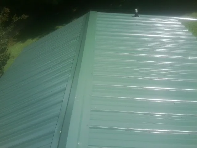 New green metal panels meeting at the ridge of a roof — Flat Roof Repair work by our crew in Allison