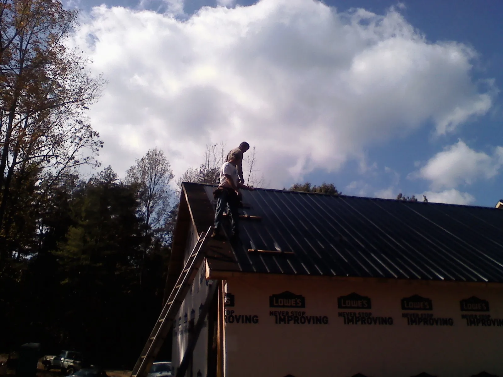 Roofer fastening dark metal panels high against a cloudy sky, from a Roof Inspection job in Allison